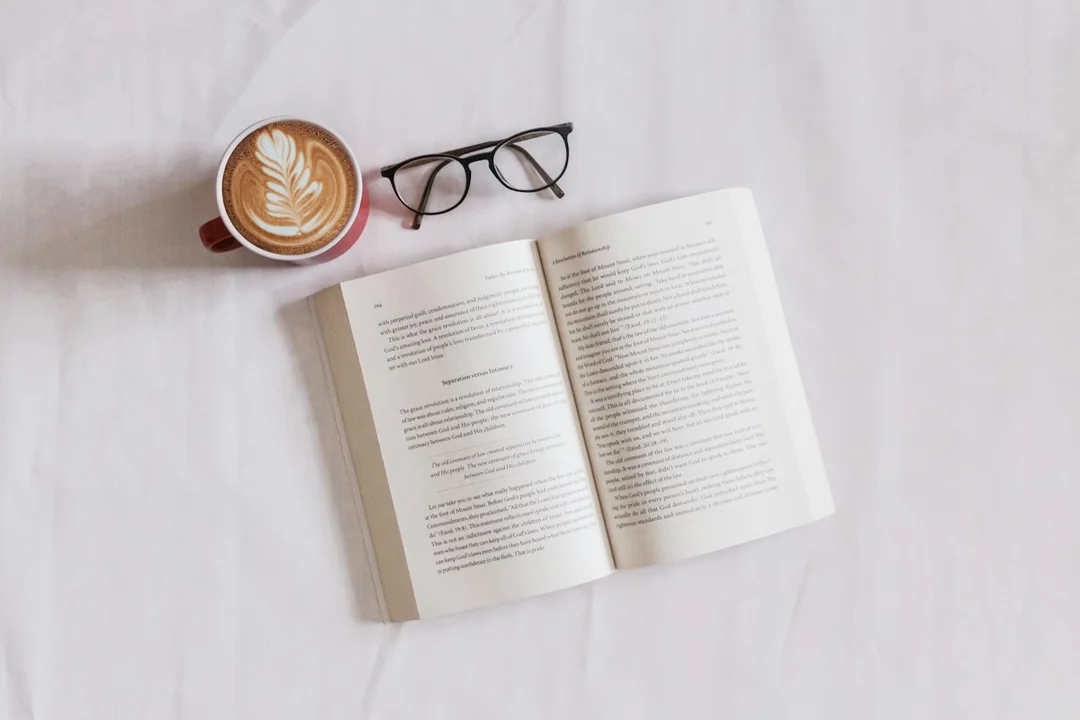 An open book, coffee and glasses on a white surface